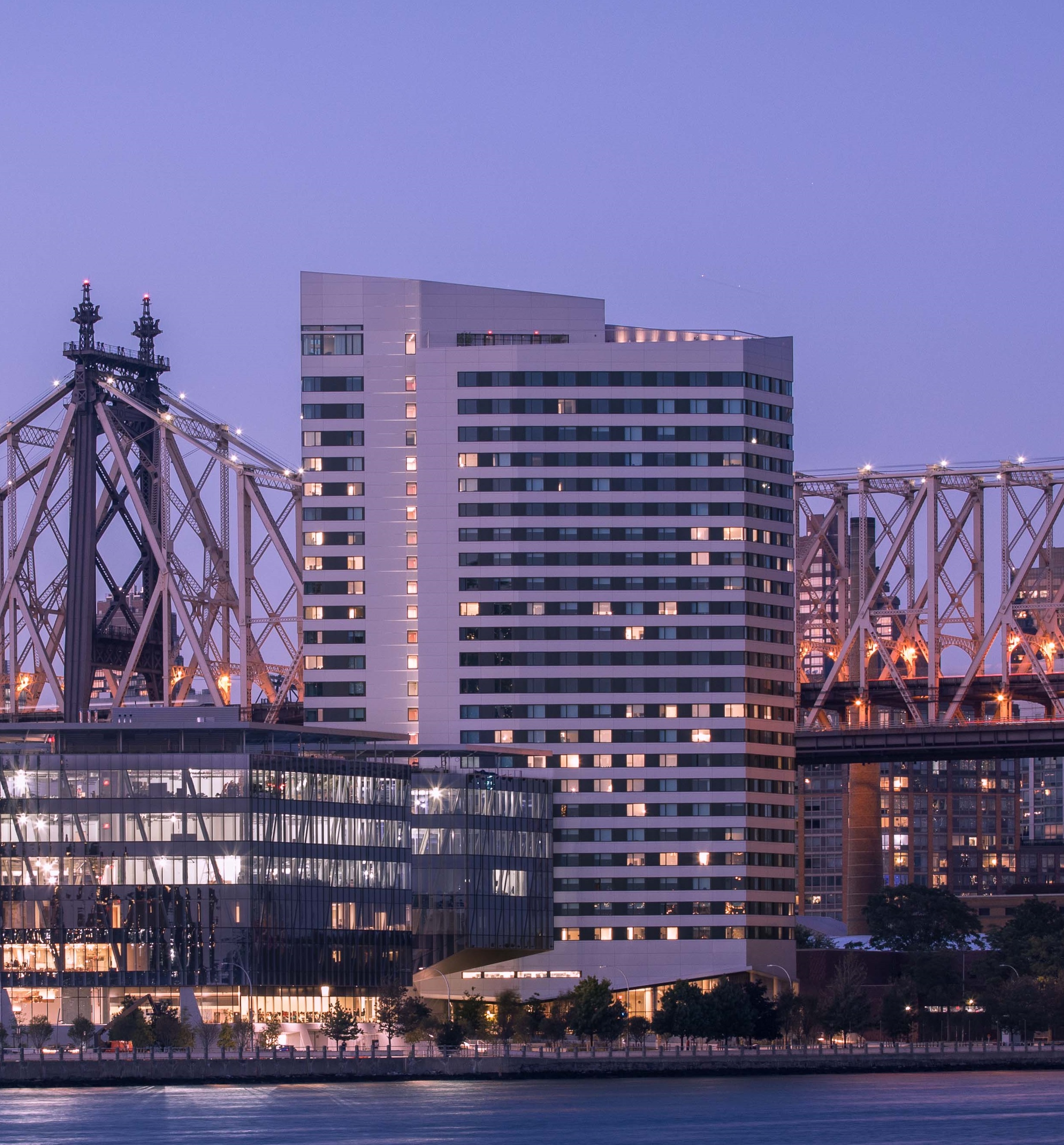 The House at Cornell Tech, a residential high-rise, at dusk with the Queensboro Bridge behind.