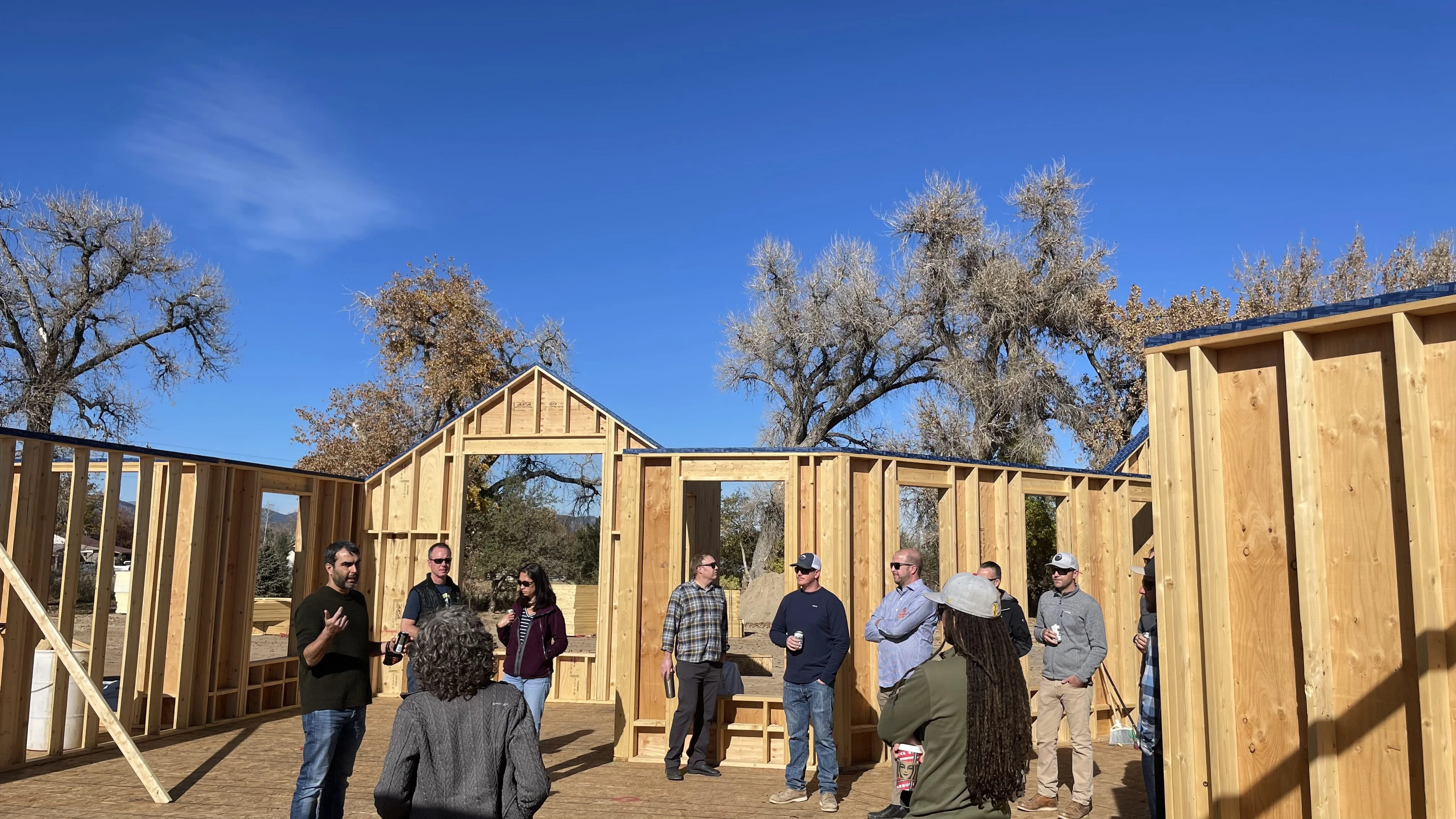 Tour group among timber wall framing under a blue sky.